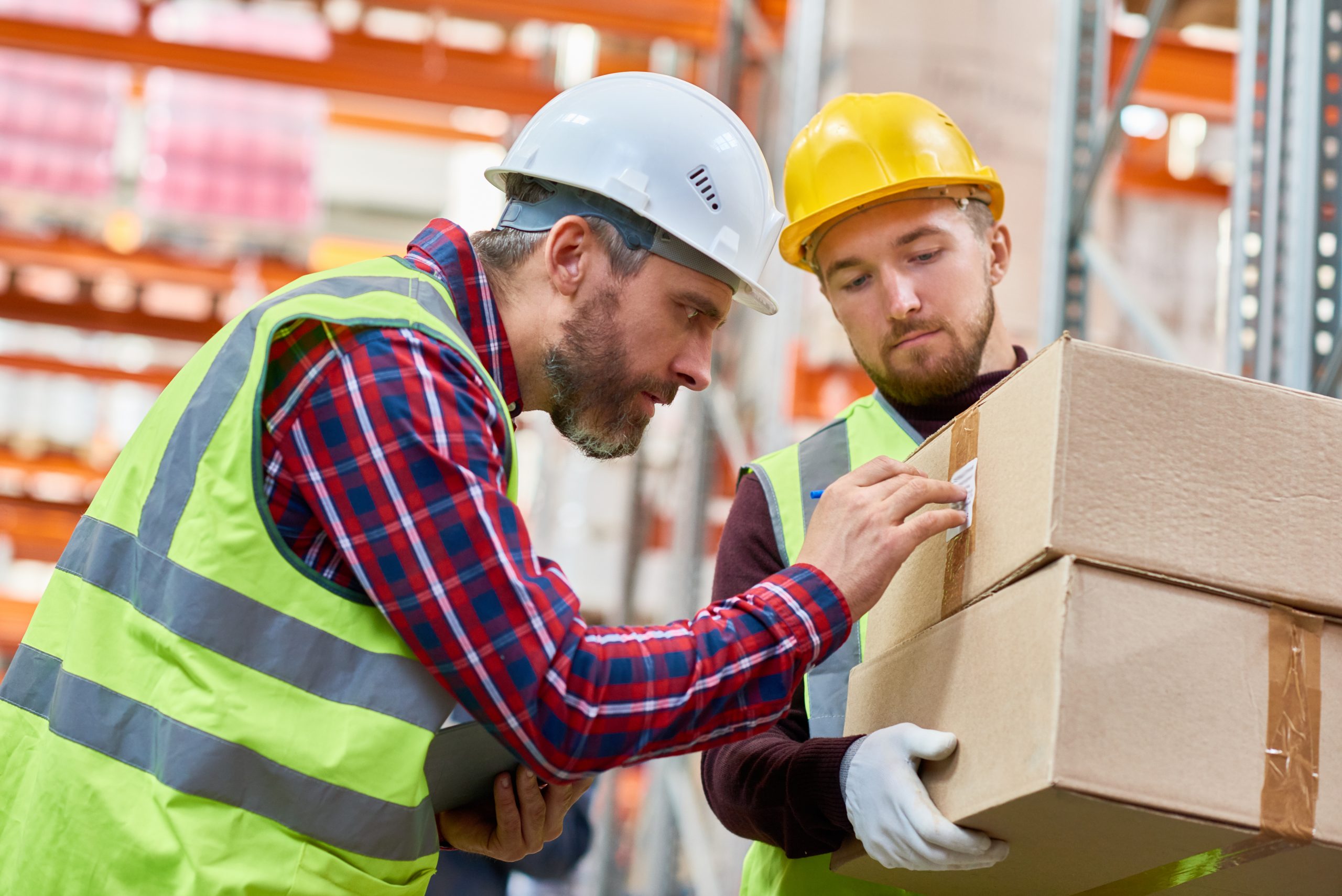 Side view portrait of two shipping workers marking cardboard box for delivery  in modern warehouse