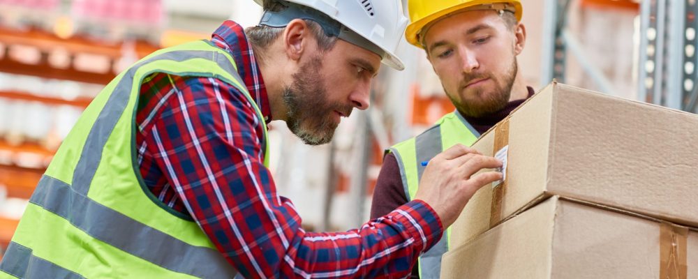 Side view portrait of two shipping workers marking cardboard box for delivery  in modern warehouse